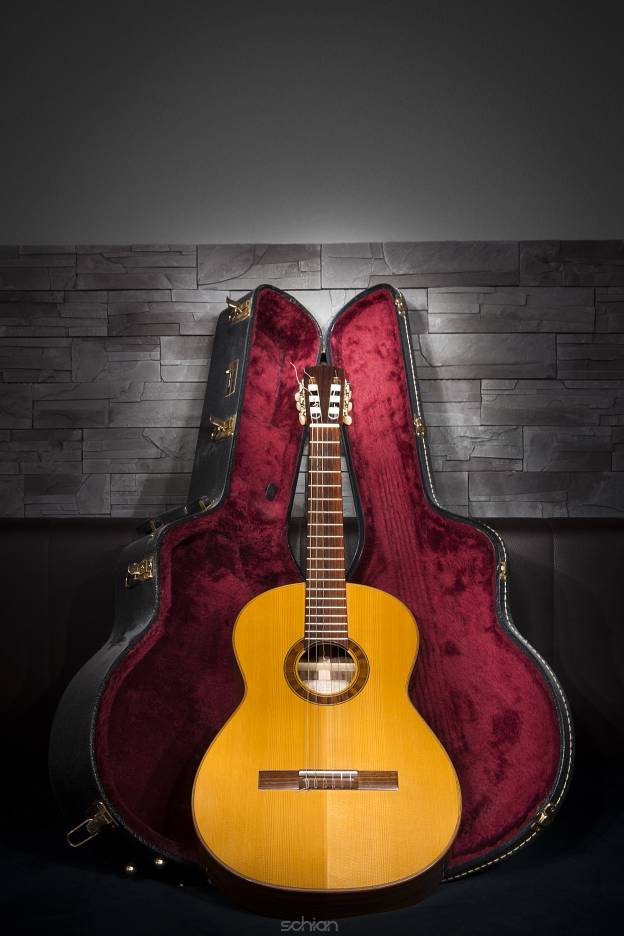 illuminated classic music guitar with case in front of leather and stone wall