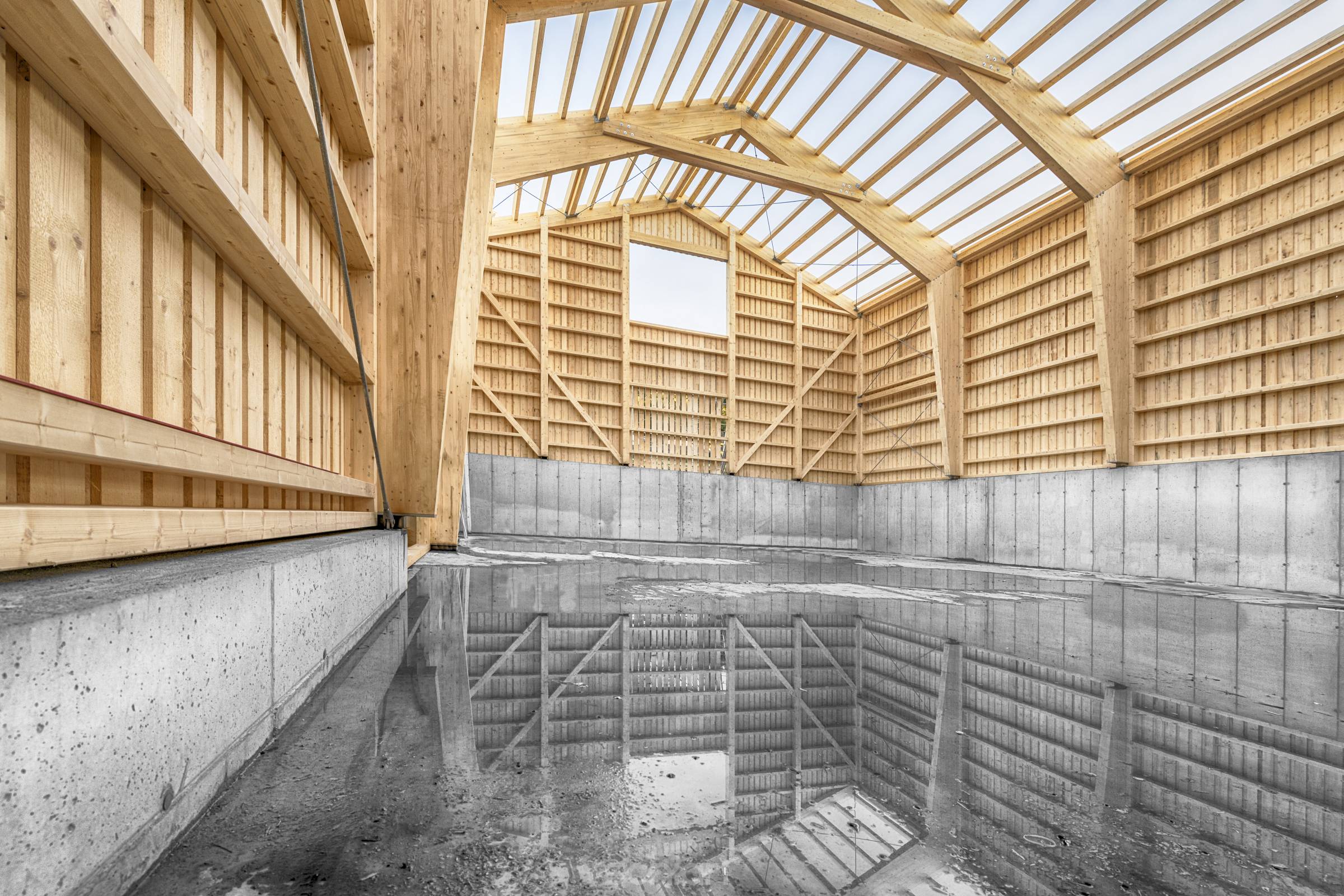 Large engineering hall in timber construction with a concrete base wall and reflection of the construction in the water