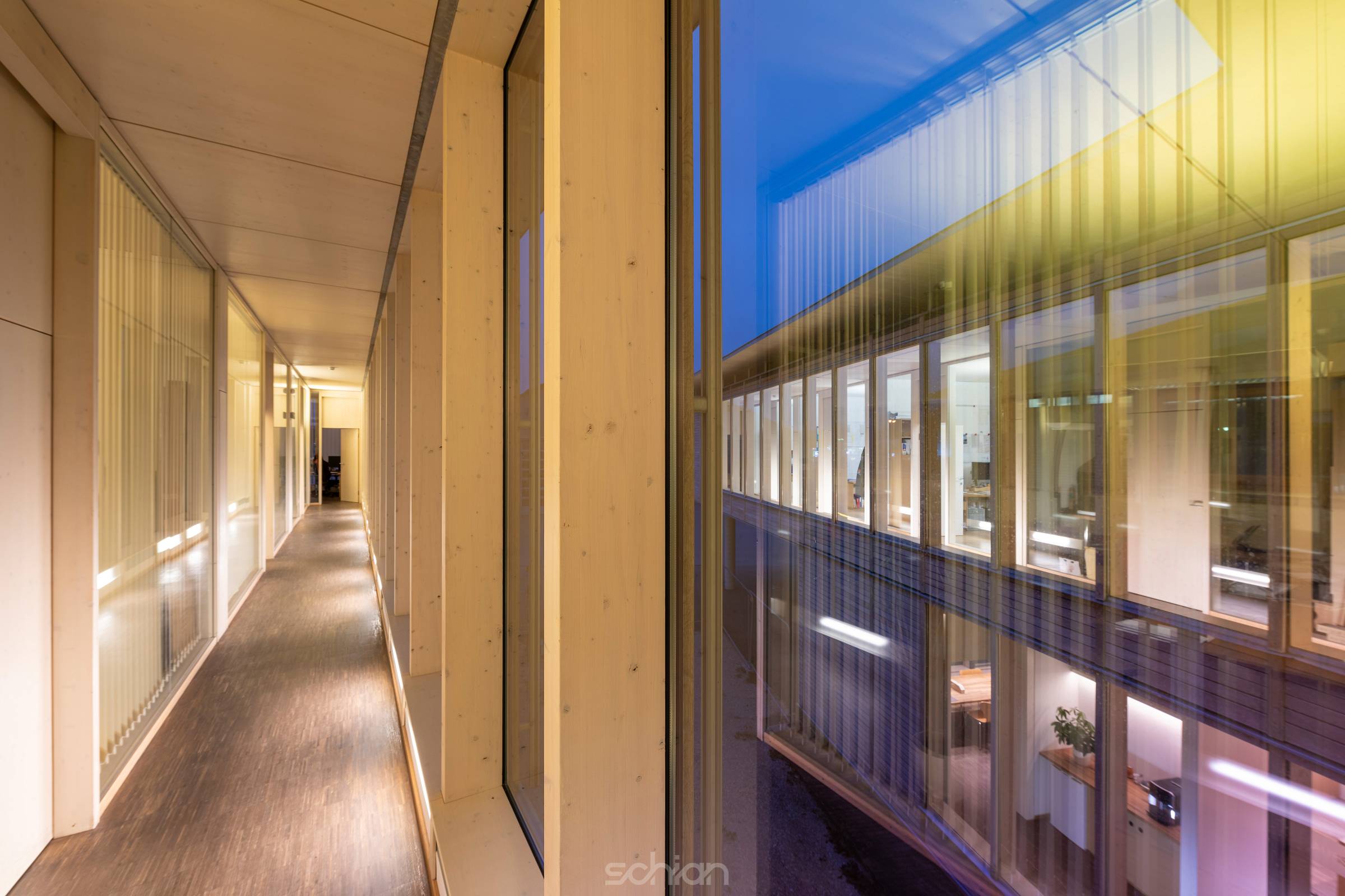 View from aisle of a wood construction office building through window to glass facade at night