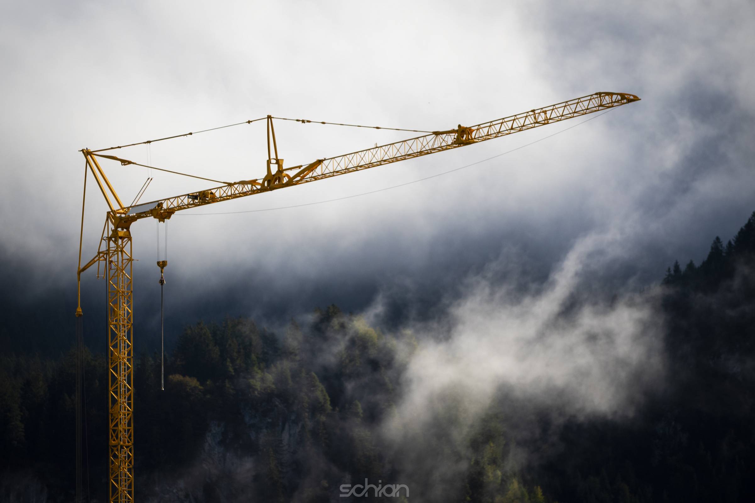 orange construction site crane with foggy misty forest in background with fading white to top