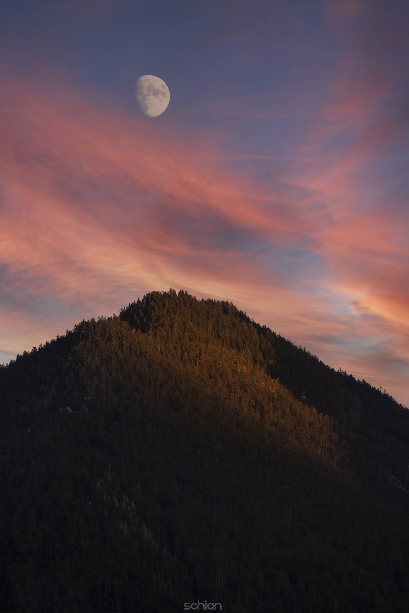 forested mountain peak with moon at sunset and burning clouds