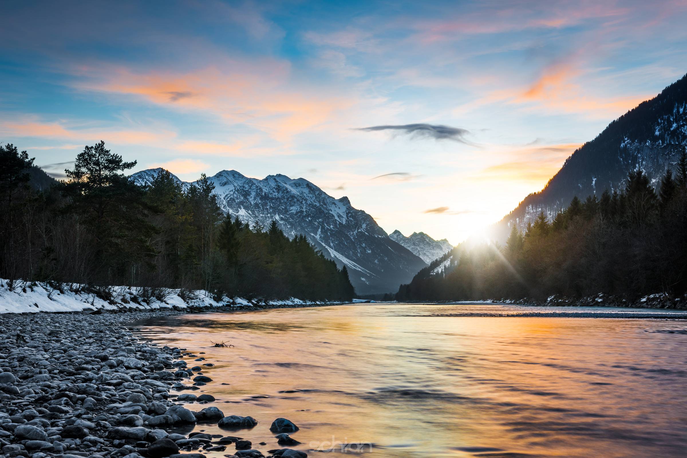 reflecting colors of sunset clouds in rural river in tirol mountains