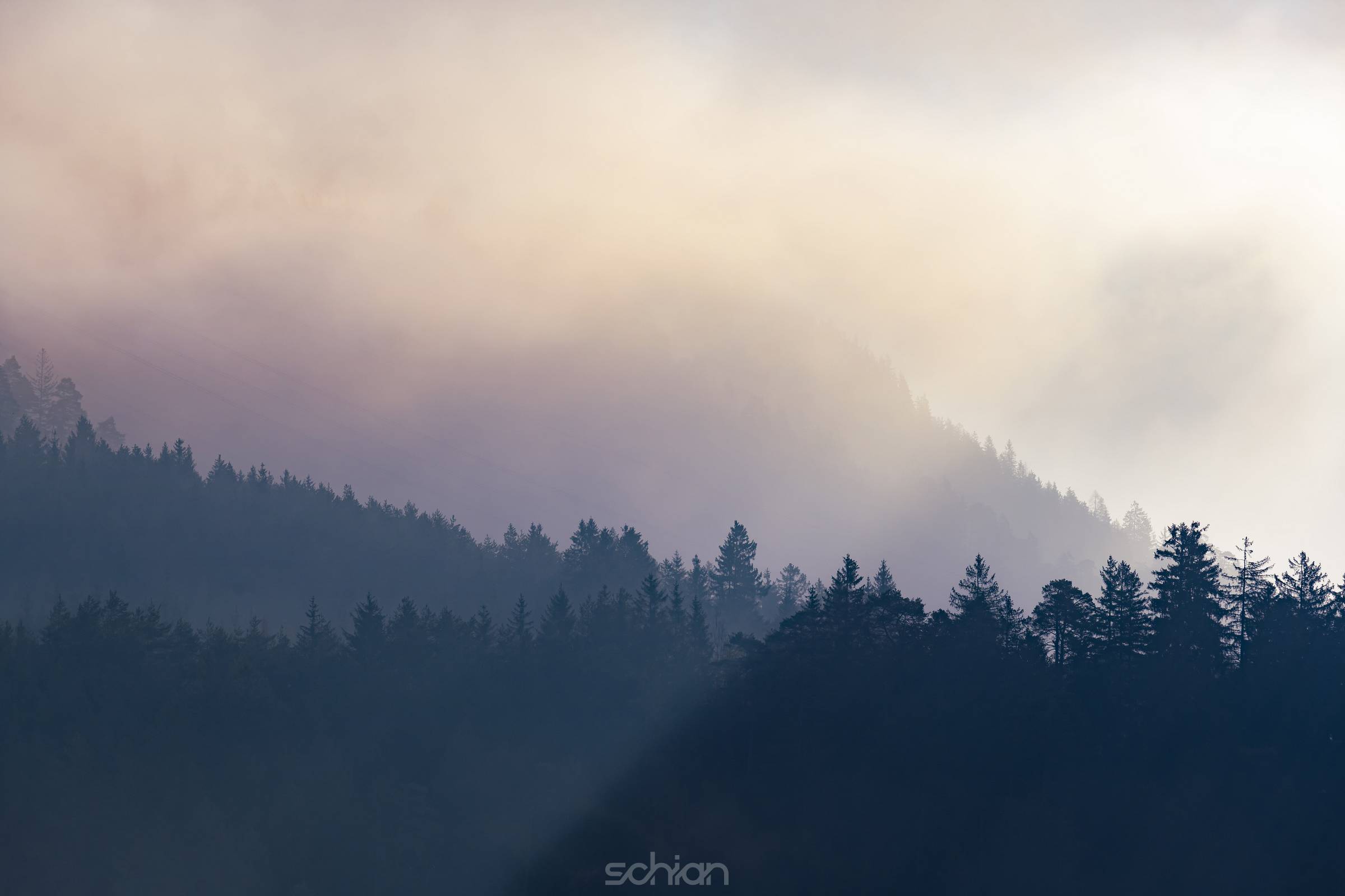 Sun rays streak three levels of misty mountain forests in autumn