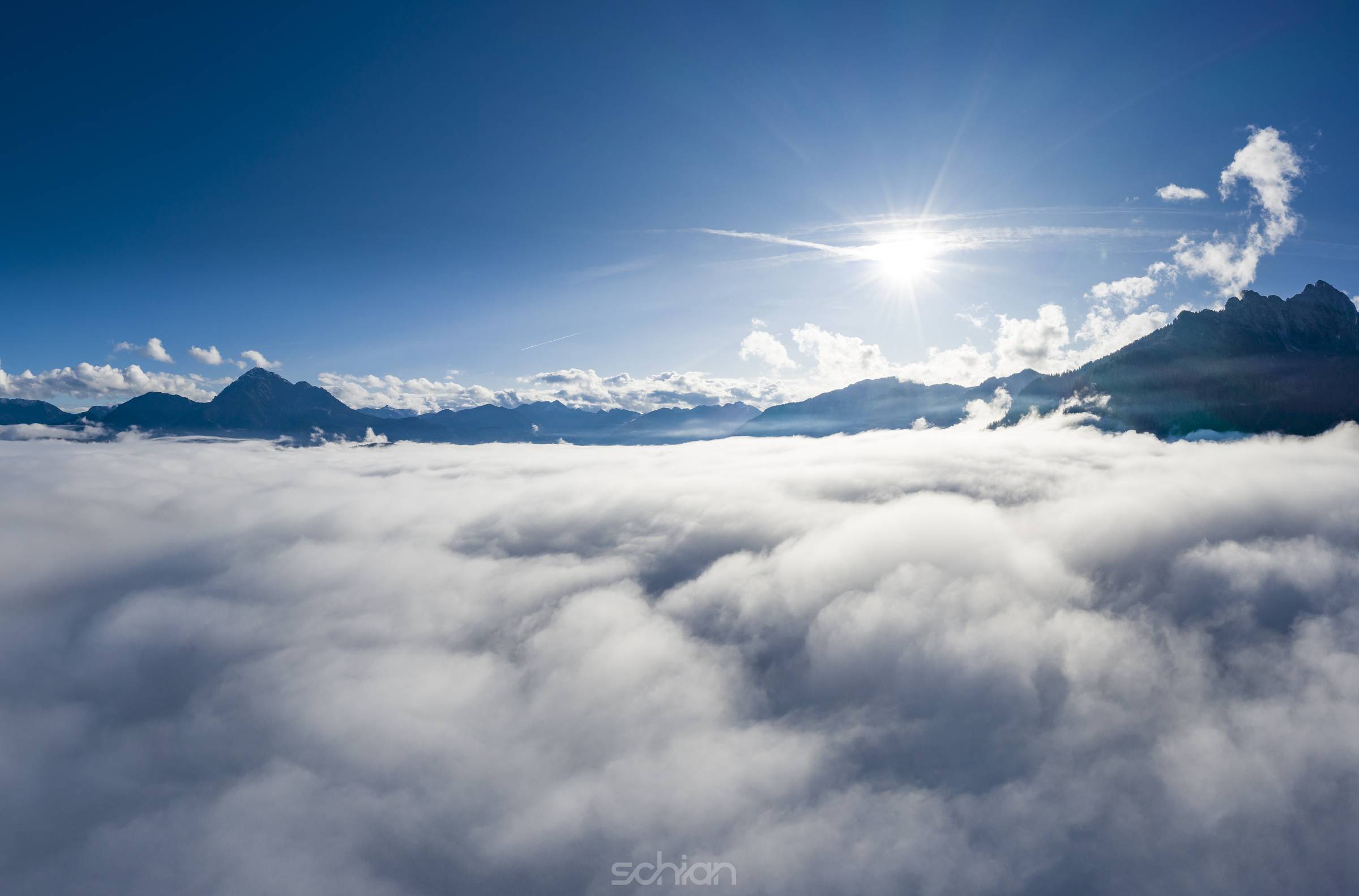 aerial view over cloud bank to tirol mountain alps with sun beams