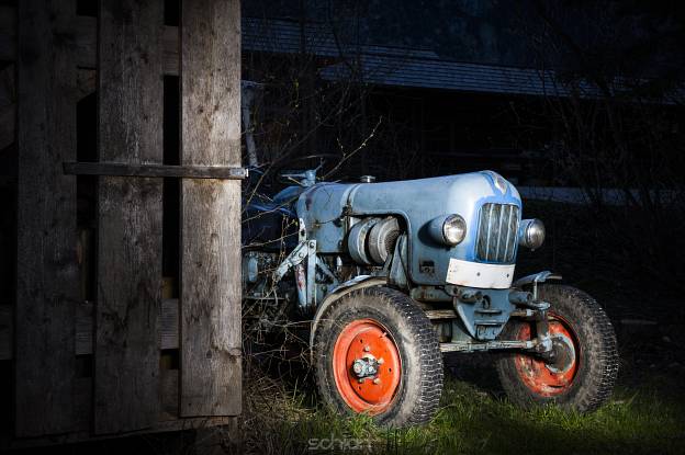 blue oldtimer farming tractor standing next to a wooden hut at night