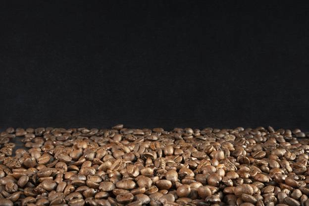 one third of freshly roasted brown coffee beans with two thirds of black background